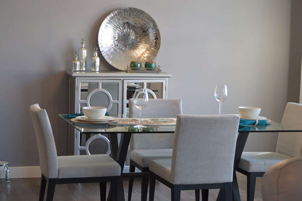Esszimmer Esstisch mit grauen Stühlen, mit weißem Porzellan eingedeckt, im Hintergrund ein weißes Sideboard mit Spiegeltüren und silberner Deko