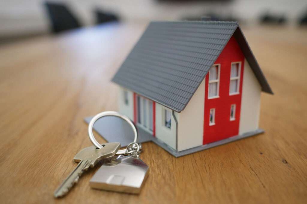 Hauskauf und Schlüssel ein kleines Modellhaus mit einem Schlüssel und einem Schlüsselanhänger auf einem Holztisch