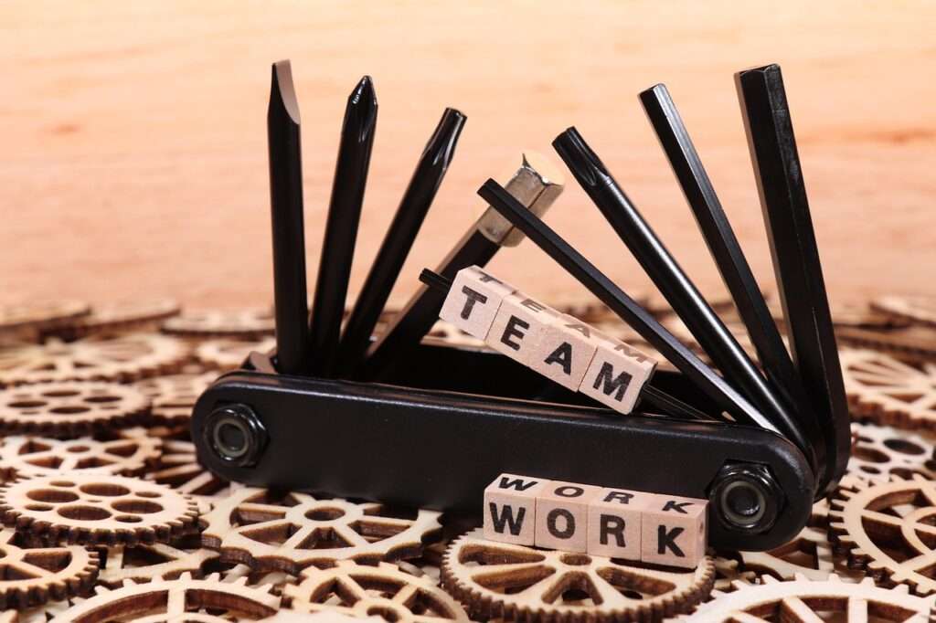 Multitool Teamwork Multitool auf einer Fläche aus Holzzahnrädern mit den Schriftzügen Team und Work